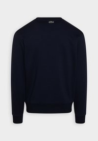 Námořnická modrá mikina, bavlněný materiál, kulatý výstřih, žebrované manžety a lem, logo Lacoste na zadní straně, hladká textura, pohodlný design.