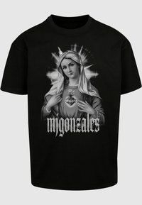 Sort bomulds t-shirt med et gråskala design af en religiøs figur med et hjerte. Teksten nedenfor siger "migonzales" i en fed skrifttype.