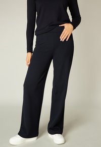 Marineblauwe wijde broek van rekbaar materiaal, met een gladde oppervlakte en een relaxte pasvorm, gecombineerd met witte sneakers.