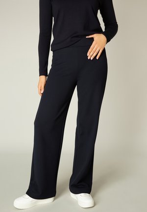 Navy wide-leg trousers in a stretchy fabric, featuring a smooth surface and a relaxed fit, paired with white sneakers.