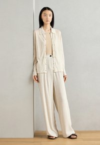Beige langermet skjorte med knapper, sammen med ribbede, vide bukser, begge i lyse nøytrale toner. Glatt tekstur, minimalistisk design.