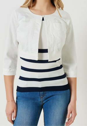 Frau trägt eine kurze weiße Jacke mit Dreiviertelärmeln über einem weiß-navy gestreiften Top kombiniert mit blauen Jeans.