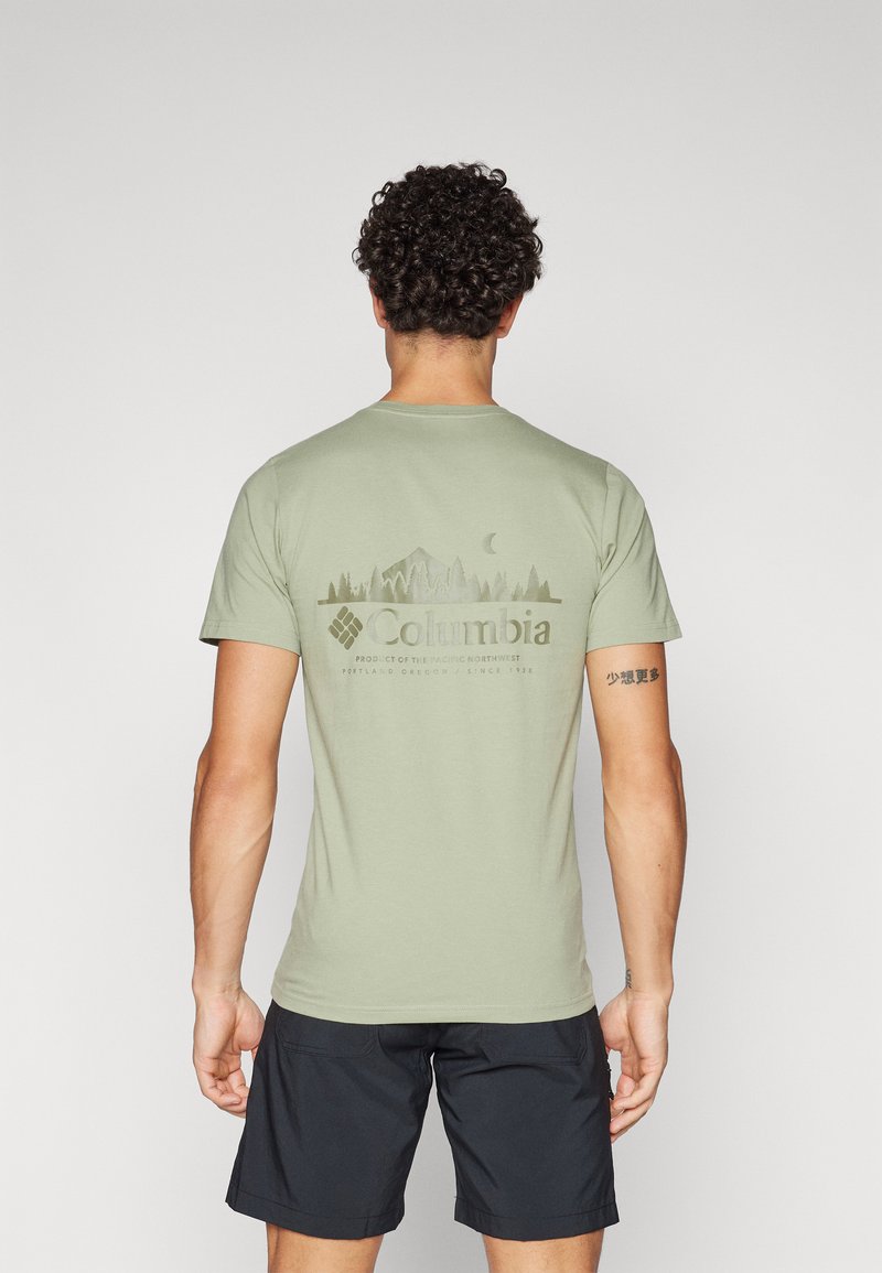 Olivengrøn t-shirt med kort ærme, der har et grafik af mountain og skov i en mørkere nuance. Teksten viser "Columbia" samt produktdetaljer nedenfor.
