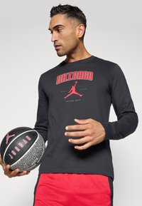 Schwarzes Langarm-T-Shirt mit rographic "CHICAGO" und Jumpman-Logo, kombiniert mit roten Sportshorts und einem schwarzen Basketball.