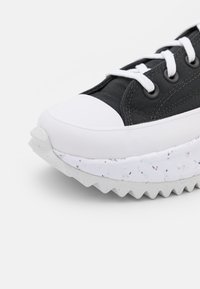 Svart canvas sneakers med vit gummikåpa och texturerad vit sula med fläckar. Snören i vitt, kompletterade av svarta öglor.