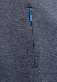 Mörkblått tyg med en mjuk textur som har en funktionell dragkedja med en ljusblå dragknapp. Sömmar synliga nära dragkedjan.