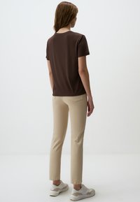 Bruine short-sleeve top gecombineerd met lichtbeige, aansluitende broek en witte sneakers. De outfit heeft een eenvoudig ontwerp zonder patronen.