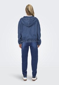 Džínová bunda s kapucí, elastickým pasem a manžetami. V kombinaci s odpovídajícími džínovými kalhotami. Oba kusy jsou modré s hladkým povrchem.