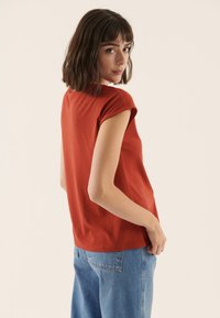 Rust-colored short-sleeve top with a relaxed fit and rounded neckline, paired with light blue high-waisted denim jeans. Simple design.