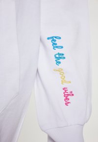 Felpa bianca con polsini a costine, caratterizzata da testo ricamato multicolore "feel the good vibes" in blu, giallo e rosa lungo le maniche.