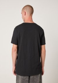 Črna bombažna majica z ohlapnim krojem, kratkimi rokavi in okroglim izrezom. Gladek tekstura, ravna podloga na zadnji strani.