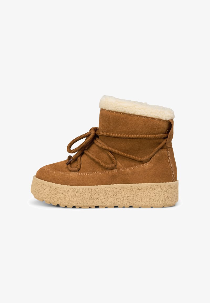 Bruine suède enkellaars met een nepbontkraag, vetersluiting en een zware beige rubberen zool met textuuraccenten en stiksels.