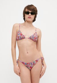 Virágmintás bikini háromszög tetejével és állítható, megkötős alsó résszel. Az anyag színes, virágmintázatú, világos háttérrel.