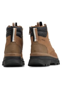 Botas de ante y textil marrón con detalles negros, cremalleras laterales y una suela de goma resistente. Presentan rayas contrastantes en la parte trasera.