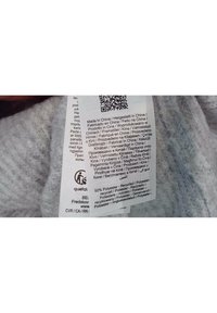 Šedá textilní etiketa s pokyny k údržbě a podrobnostmi o materiálu; 50% recyklovaný polyester; tištěno v několika jazycích; zahrnutý QR kód.