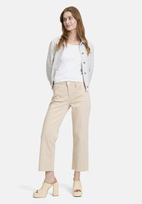 Jasnoszary teksturowany żakiet z niebieskimi guzikami, biały top bez rękawów, beżowe spodnie o kroju 7/8 oraz kremowe mule na blokowym obcasie. Prosty design bez wzorów.