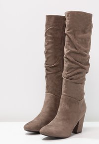 Brown suede knee-high boots with a slouchy design, pointed toe, and a chunky heel. Features a side zipper for easy wear.