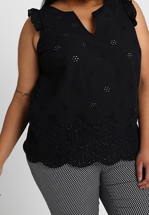 Czarny top bez rękawów z kwiatowymi wzorami ażurowymi i falistym dołem, skomponowany z czarno-białymi kratkowymi spodniami na osobie.