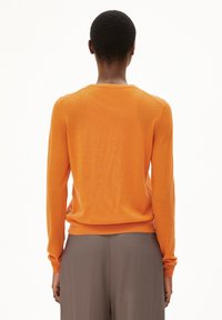 Orange knit sweater with long sleeves and a round neckline. Features a relaxed fit and ribbed cuffs. Worn over gray pants.
