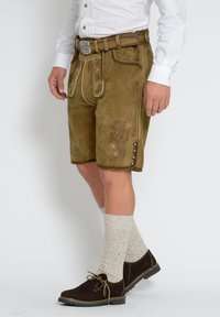 Bruna mockaskorts med blommig broderi, knappdetaljer och pipingdetaljer, tillsammans med grå stickade strumpor och mörka skor.