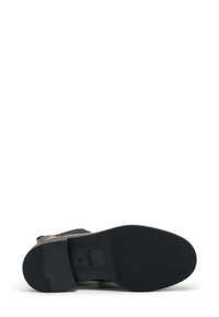 Suela de zapato de goma negra con superficie texturizada, presenta una parte superior de cuero marrón con un acabado suave y un sutil detalle de diseño.