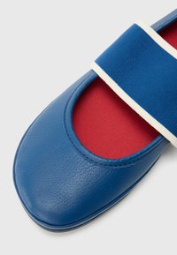 Modrý kožený balerín s červeným vnitřkem a modrým elastickým páskem s bílým akcentem. Hladká textura a kulatá špička.