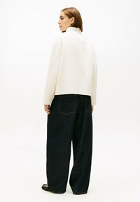 Roomkleurige, losvallende trui met hoge kraag, gecombineerd met donkerblauwe denim broek met wijde pijpen, achterzakken en subtiele stiksels.