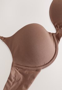 Pruun polsterdatud rinnahoidja, millel on sile kangas, vormitud korvid ja reguleeritavad rihmad. Disainil on õmbluseta viimistlus ja klassikaline haaklukk.