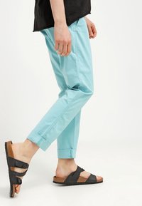 Ljusblå, avsmalnande bomullsbukser med upprullade fållar, parat med svarta halksandaler med korksula och två vävda remmar.