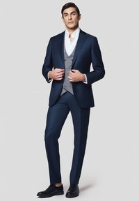 Granatowy garnitur skrojony na miarę z szarym kamizelką, białą koszulą i czarnymi butami. Posiada dopasowany krój, wyraźnie zarysowane ramiona oraz delikatny połysk.
