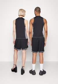 Schwarze sportliche Tanktops mit grauen Akzenten, kombiniert mit schwarzen Shorts mit weißen Details. Sichtbares Schuhwerk umfasst High-Heelsandalen und Turnschuhe.