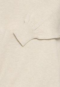 Világos bézs kötött pulóver ujj, bordázott mandzsetta részlettel. Puha textúra, enyhén felfújt forma. Kiemelve a varrás és a szövetszerkezet egyenletessége.