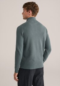 Megztinis, minkštos tekstūros, žalsvai mėlynos spalvos, aukštu apykakle, ribuotomis rankogaliais ir apačia; turi subtilų raštą. Dėvimas su kasdienėmis kelnėmis.