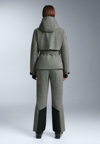 Szürke mintás külső ruházati szett, amely egy testhezálló kabátból és bővülő nadrágból áll. A kapucnis kabát derékban összehúzott, míg a nadrág fekete kontrasztos kiegészítőkkel rendelkezik.