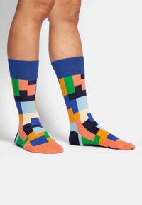 Bunte knielange Socken mit einem blauen Bündchen, das ein geometrisches Muster in Orange, Blau, Grün und Schwarz auf einem hellen Hintergrund zeigt.
