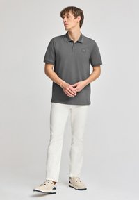 Grå polo t-shirt med krage och tre knappar, texturerad tyg, kombinerad med vita byxor och beige sneakers med mörka accenter.
