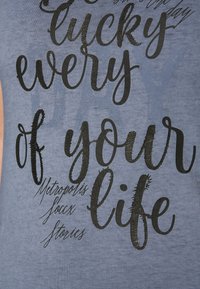 Blue cotton tank top featuring large black text that reads "Lucky every of your life" with a smaller text below "Metropolis" and "Soçy Stories."