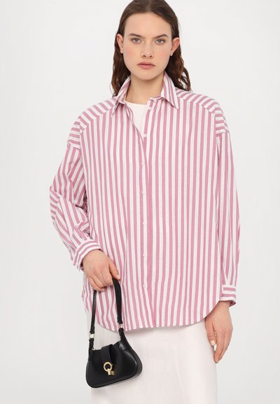 Chemise boutonnière à rayures roses et blanches avec un col, des manches longues et une coupe décontractée, associée à un petit sac à main noir avec un accent doré.