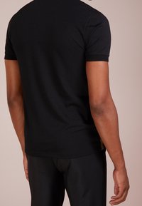 Schwarzes Kurzarm-T-Shirt mit glatter Textur, featuring einem gestickten Halsausschnitt und einem dezenten Logo-Highlight an der Seite.
