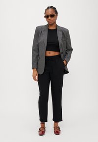 Grått houndstooth-blazer over en svart crop top, kombinert med svarte drawstring-bukser og røde lakkledds-flats med ankelstropper.