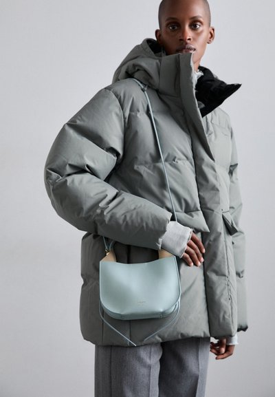 Veste grise matelassée avec capuche, doublure noire ; sac à main en cuir bleu clair avec des accents beiges ; pantalon gris ; texture douce.