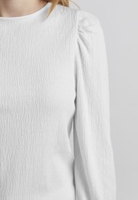Weißes Langarmshirt aus strukturiertem Stoff mit gerafften Schultern und rundem Halsausschnitt. Einfaches und elegantes Design.
