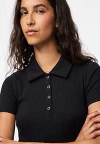 Czarna prążkowana koszulka polo z krótkimi rękawami, wyposażona w listwę na guziki z elementami w kolorze srebrnym oraz płaski kołnierzyk.