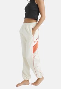 Krämfärgade sweatpants med elastisk midja, röda detaljer och "ROXY"-logotyp. Har sidofickor och avsmalnande, ribbade anklar.