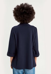 Haut bleu marine à manches trois-quarts, coupe décontractée avec poignets repliés, doté d'une texture de tissu lisse et d'un design minimaliste.