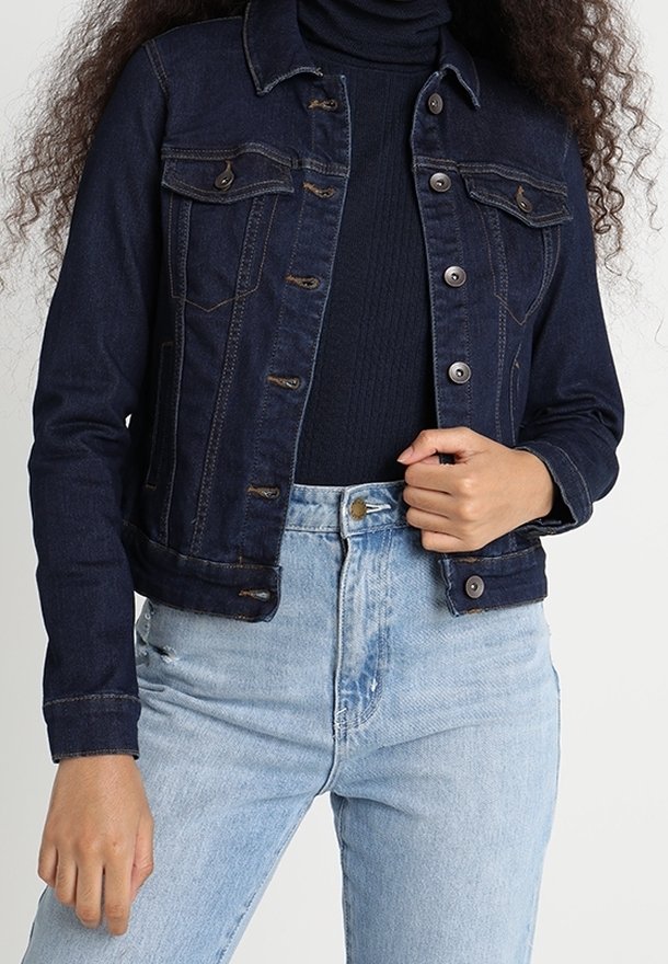 Dark blue denim jacket with a fitted design, button closure, two chest pockets, and a collar. Worn over a dark turtleneck sweater.