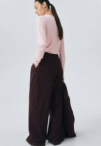 Light pink long-sleeve sweater paired with dark burgundy wide-leg trousers. The sweater has a round neckline, and the trousers feature a high waist.