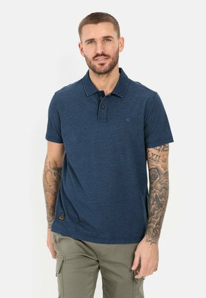 Marineblauwe polo met korte mouwen met een subtiele textuur, knoopsluiting en logo-details, gedragen met olijfgroene cargobroek.