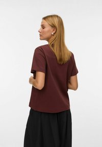 Bordowa koszulka z krótkim rękawem o luźnym kroju, wykonana z miękkiej tkaniny o prostym wzornictwie. Noszona z czarnymi, plisowanymi spodniami.