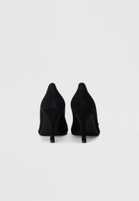 Svarte høyhælte sko i semsket skinn med spiss tupp og slank stiletthel; glatt tekstur uten synlige mønstre eller pynt.